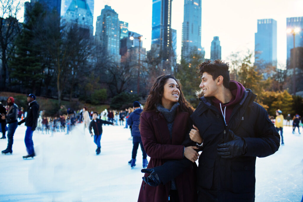 Portrait of a happy young couple smiling, holding hands and looking at each other while ice skating outside in Central Park, NYC